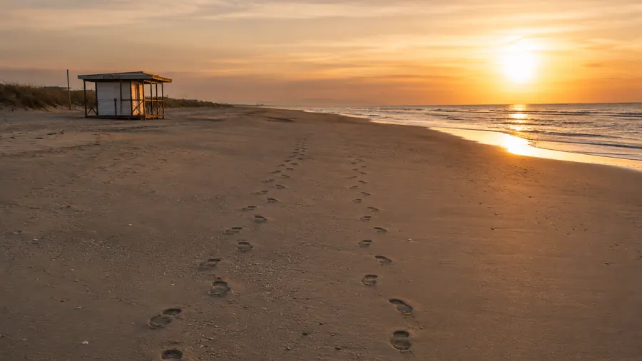 Una spiaggia deserta al tramonto con due file di impronte